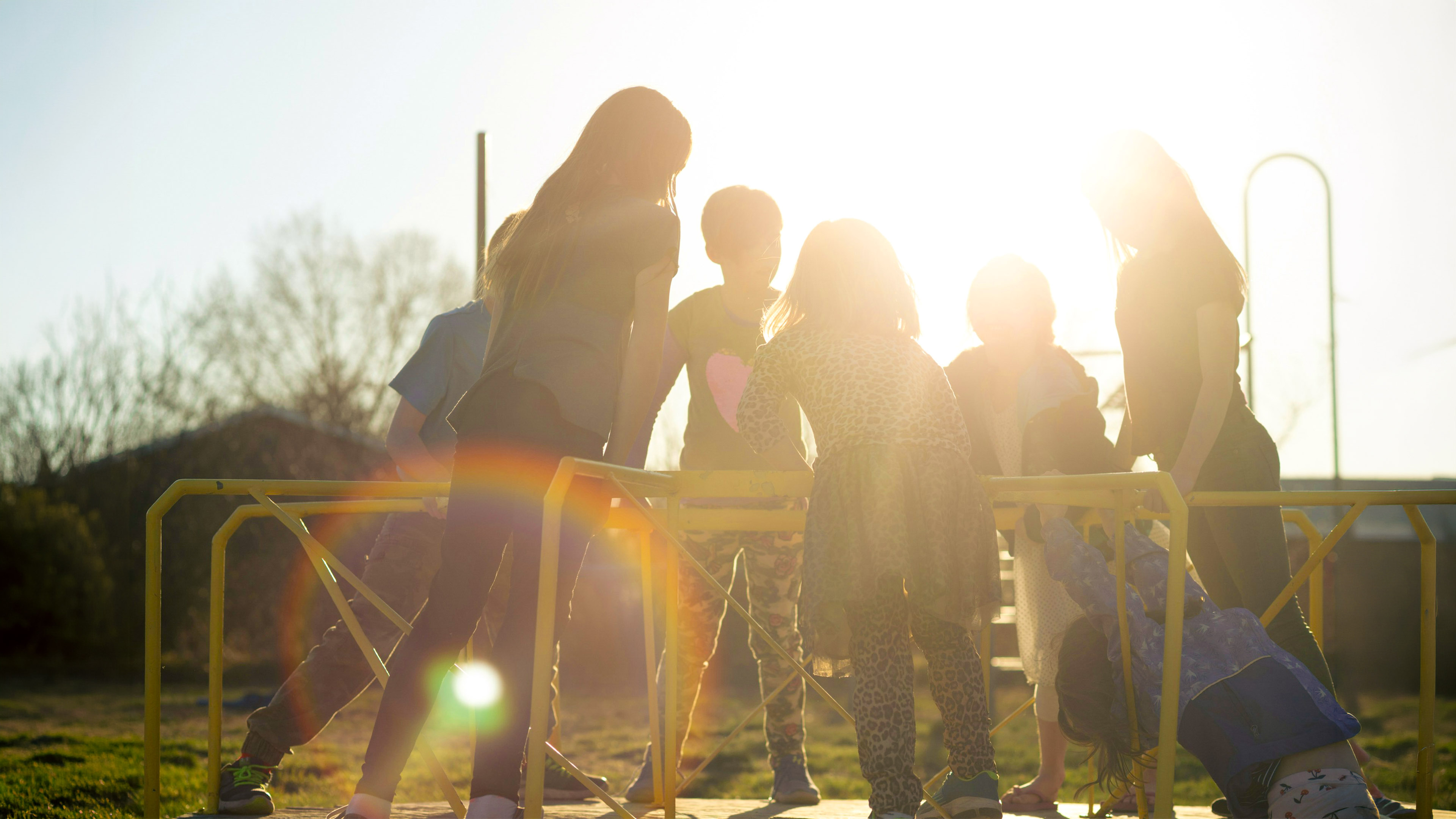 Children playing on playground equipment outdoors, silhouetted by bright sunlight.