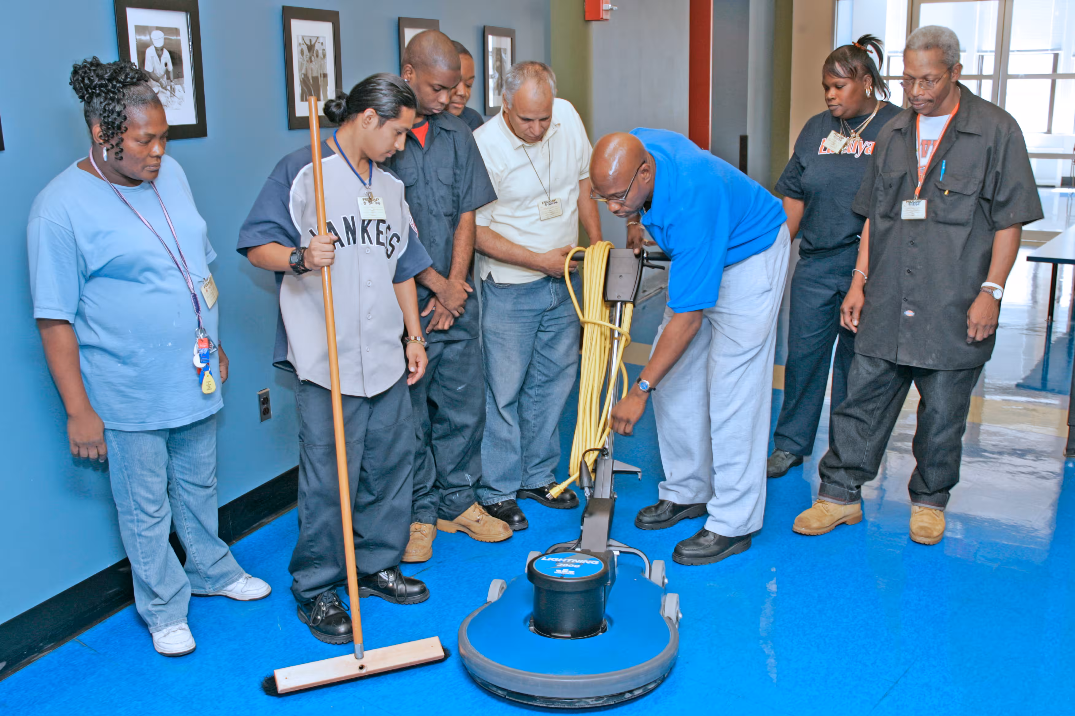 Custodial instructor leaning in to show something to a group of smiling students wearing yellow ear protection.