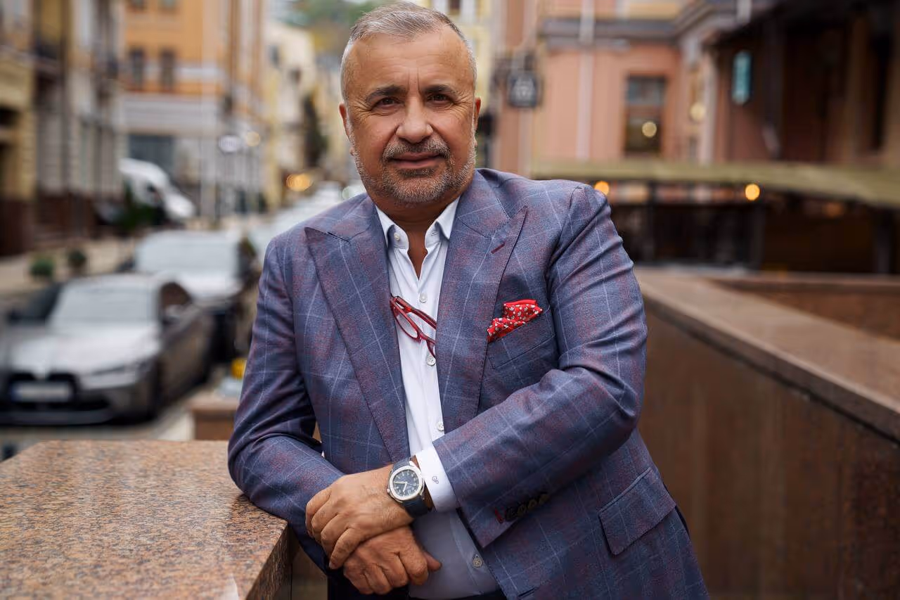Gennady Perepada man in a blue plaid suit leaning on a stone ledge on a city street.