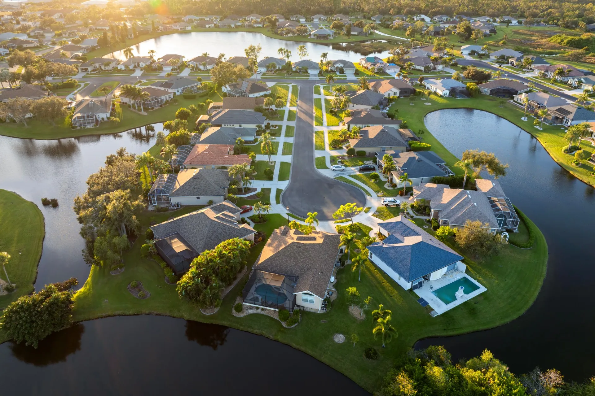 Aerial view of suburban neighborhood with houses, lawns, and water bodies surrounding the homes.