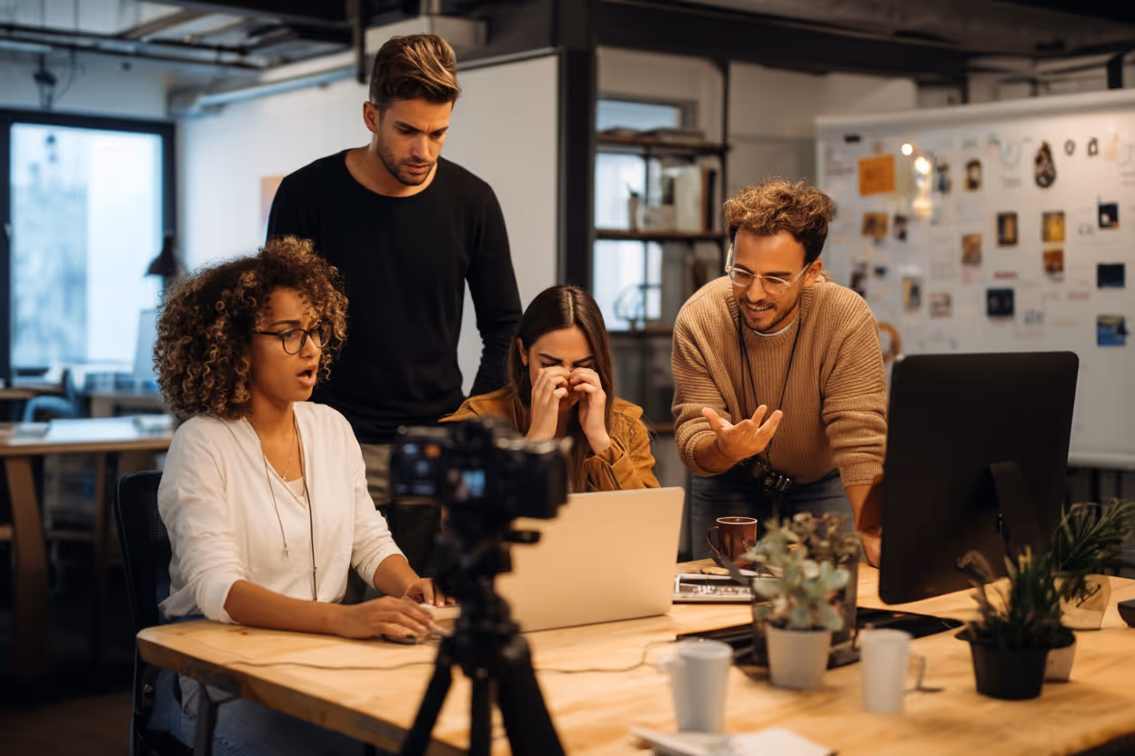 Four young professionals collaborating at a desk with a laptop and camera in a modern office.