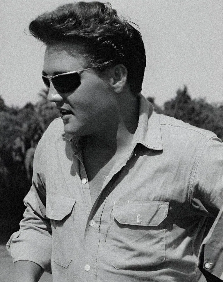 Elvis Presley de profil, portant les lunettes de soleil Solamor. Modèle Sport 1000. il est vêtu d'une chemise ouverte.
