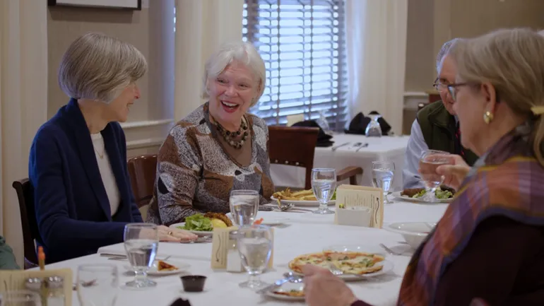 A group of Laurelmead residents enjoy lunch together at a well-set dining table. Laughter and conversation flow easily, capturing the warm, social spirit of the community.