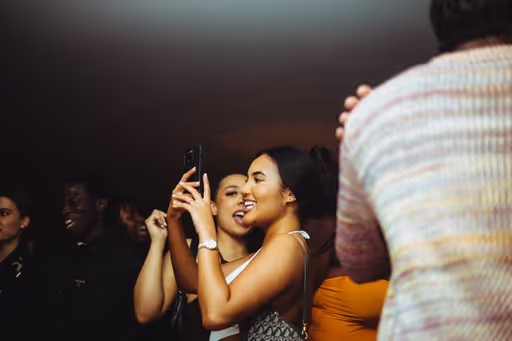 Two young women smiling and taking photos with the crowd in the background at Soirée's collaboration party with Brighton Beach House in Brighton, UK
