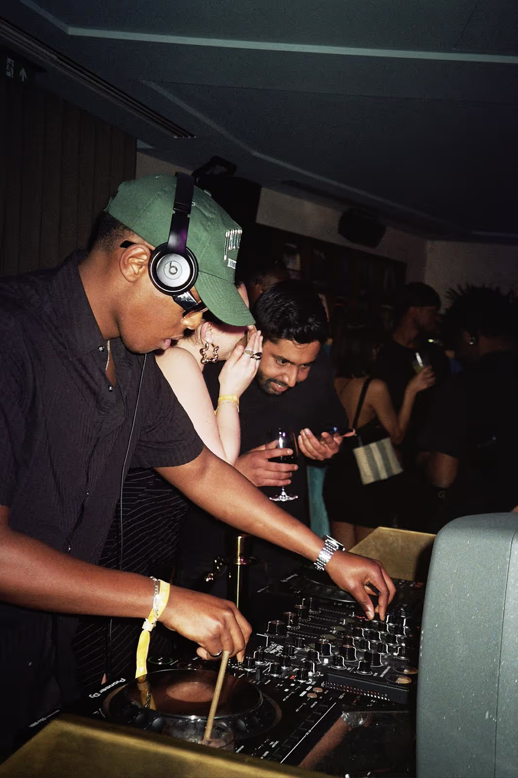 A DJ playing his set with people having fun in the background at the art show by Soirée at Soho Brighton Beach, UK