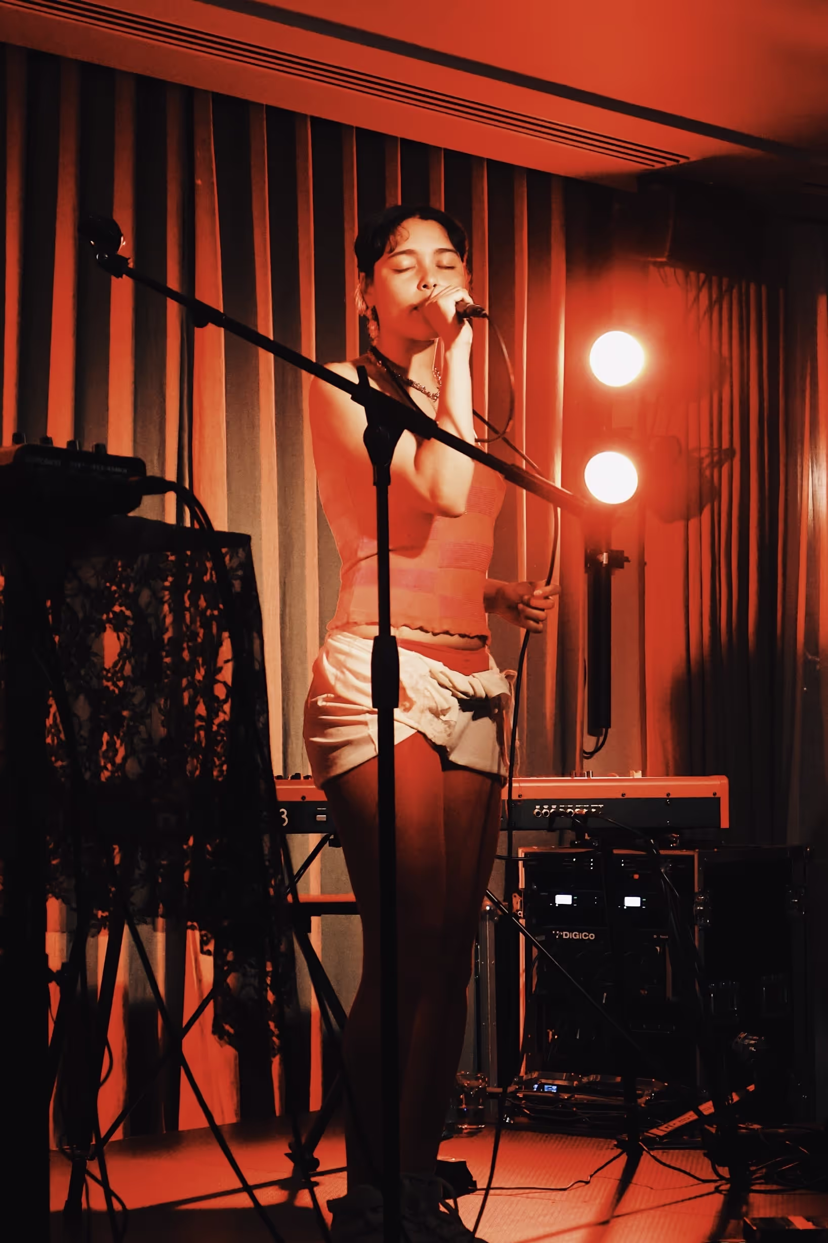 A singer performing with music gear and red lights in the background at the Soirée & GRADUATION Records collaboration event at Beach House, Brighton, UK