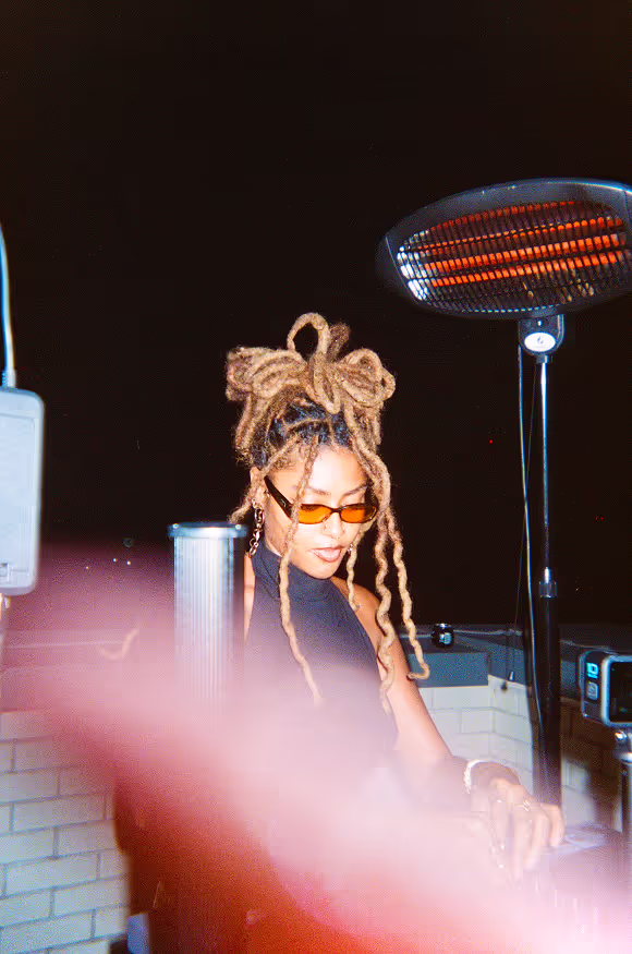 A young DJ woman with dreads playing her set at a rooftop party by Soirée in London, UK