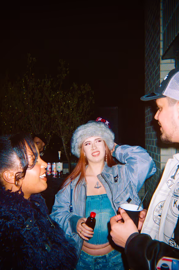 Three stylish young people talking at a rooftop party by Soirée in London, UK