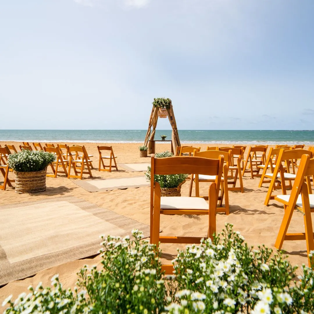 A wedding ceremony setup at the beach with beautfiul flower arrangements and wooden chairs at Wyndham Grand Rio Mar's pristine beach