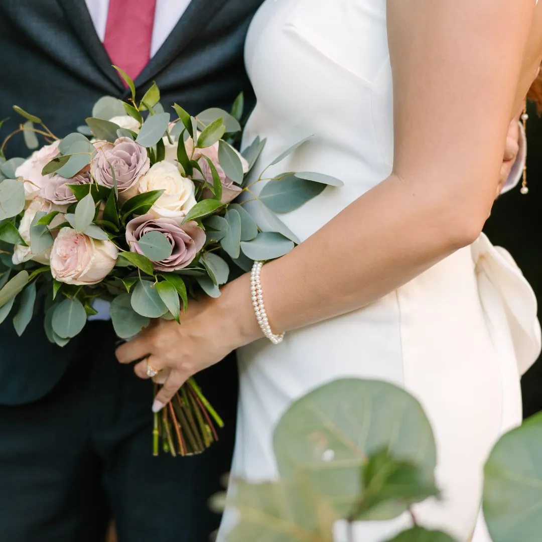 A close up image of bride and groom. the bride is holding a bouqet and dressed in her wedding dress. 