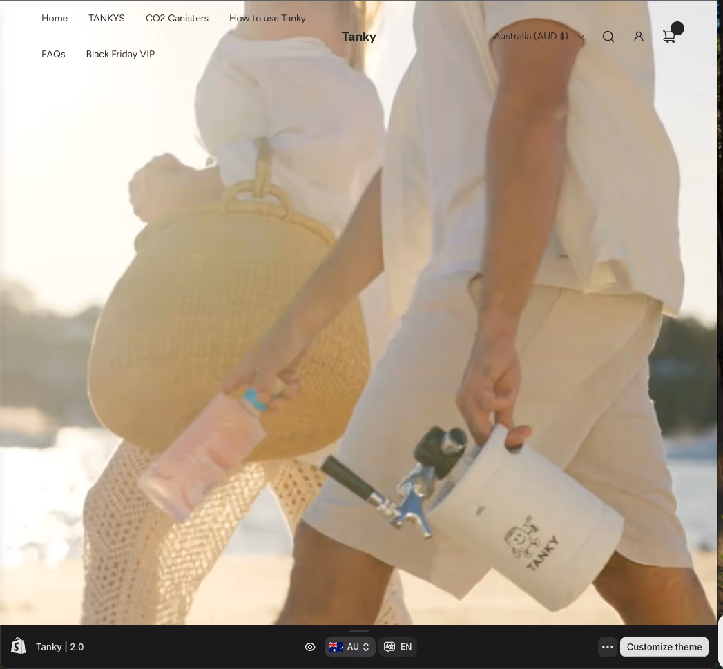 Two people walking on a sunny beach carrying a pink water bottle and a white CO2 canister labeled Tanky.