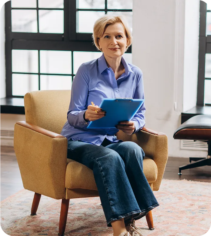 Smiling therapist sitting in an armchair with a clipboard and pen during a session.