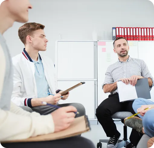 Therapist leading a group therapy session with participants taking notes.
