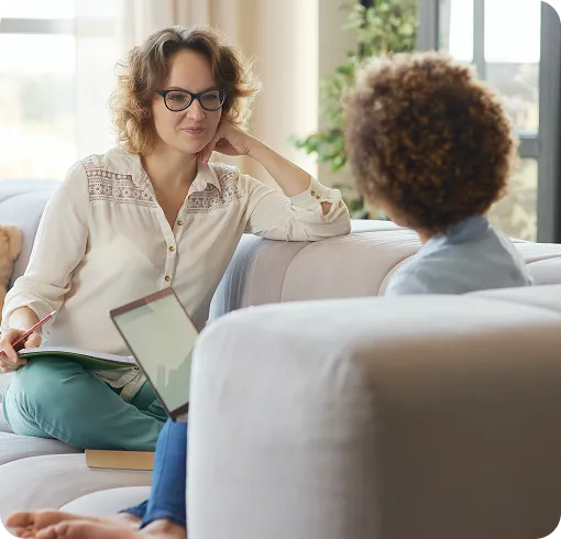 Therapist with glasses talking to a child during a counseling session on a sofa.

