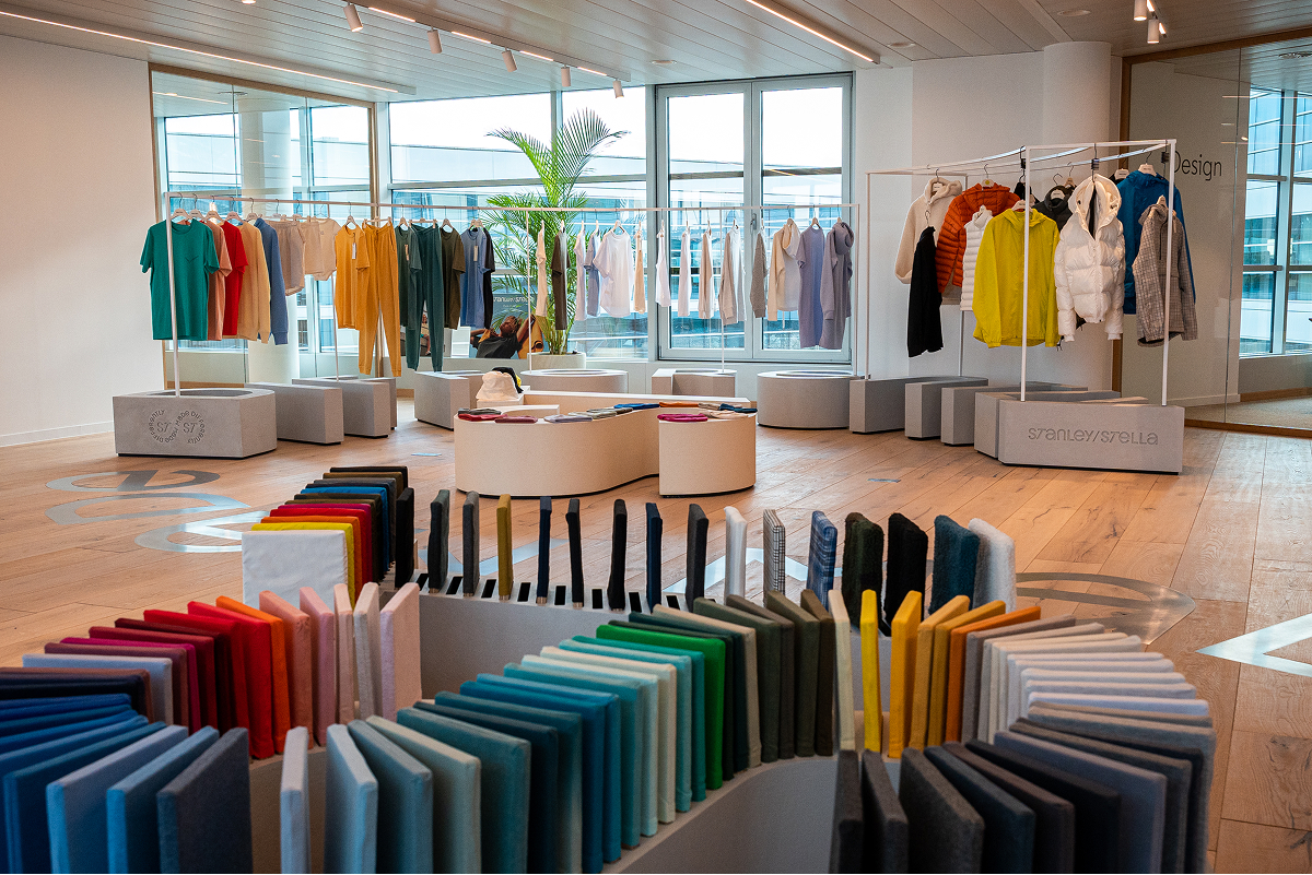 Modern showroom with colorful fabric samples arranged in a spiral in the foreground and racks displaying various clothing items near large windows.