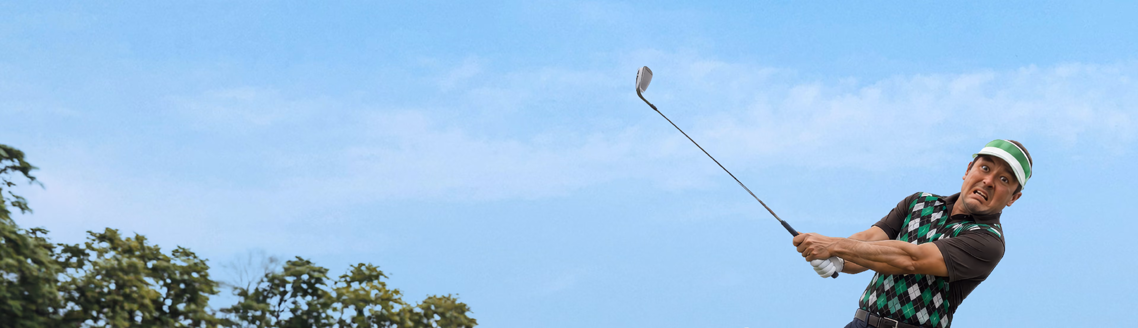Man in a green and black argyle vest, black shirt, white glove, and green visor swinging a golf club with a tense or worried expression against a blue sky with trees below.