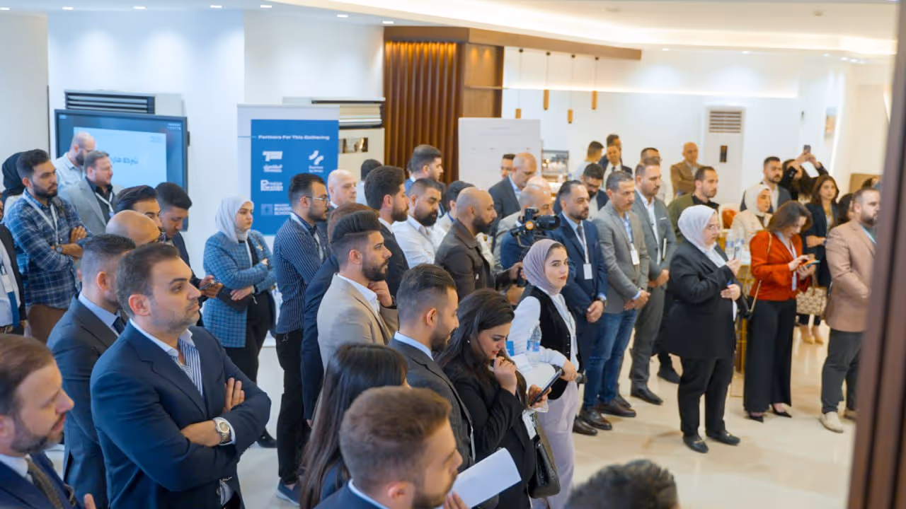 A group of people in business attire attentively listen to a speaker in a conference room.