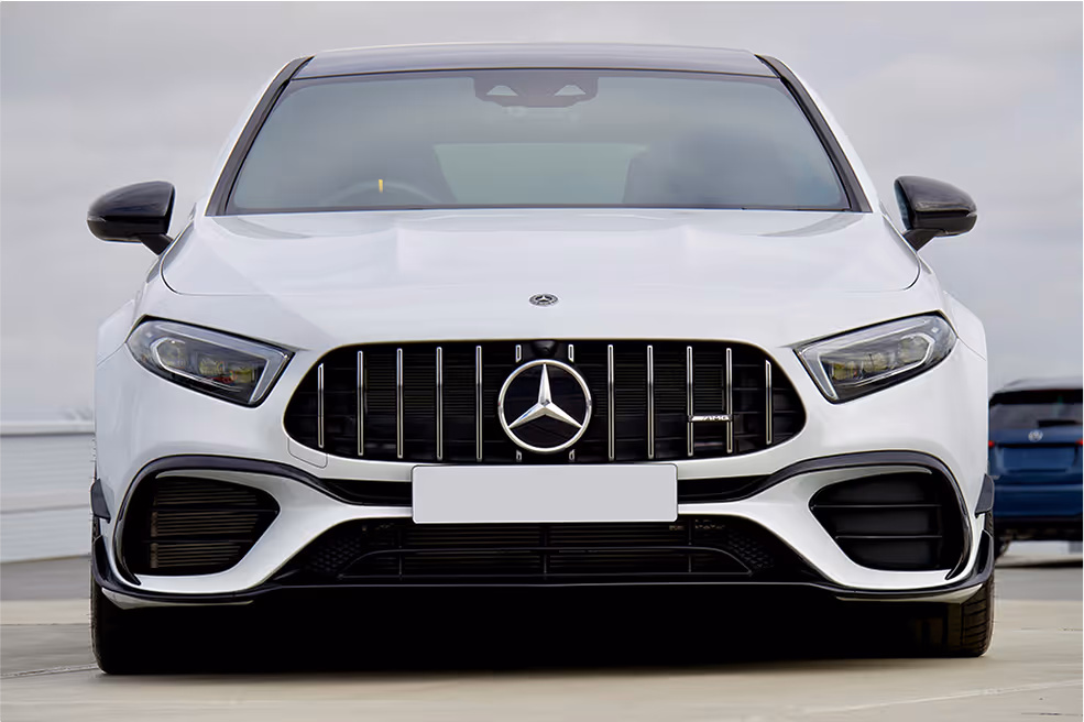 Front view of a white Mercedes-Benz car with prominent grille and headlights on a paved surface.