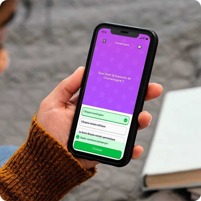 Une personne tient un smartphone affichant un quiz sur Charlemagne avec la question et trois options de réponse en français.