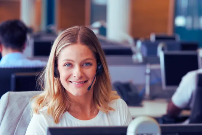 Une conseillère clientèle souriante, casque-micro sur la tête, dans un centre de relation client