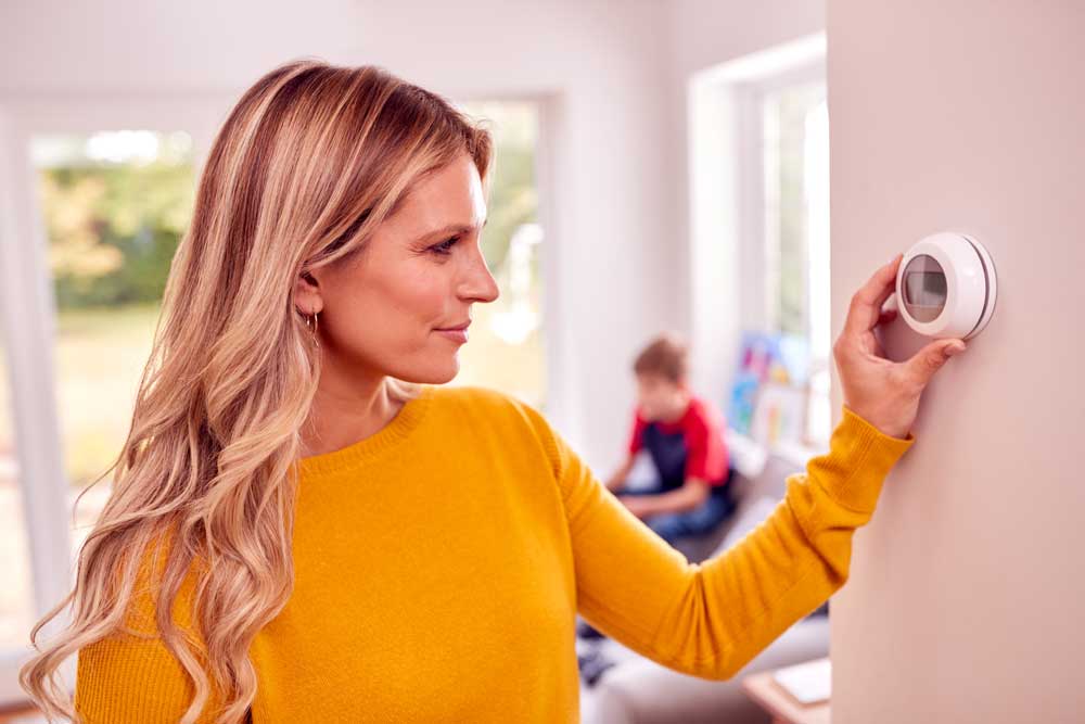 A woman adjusting smart thermostat at home during hot summer days