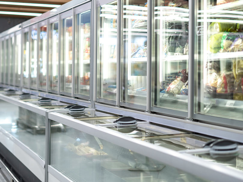 Glass-door commercial freezers stocked with frozen foods in supermarket aisle