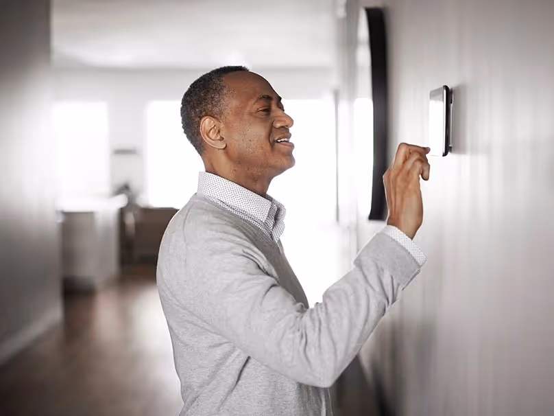 A man stands in front of a wall, adjusting a thermostat mounted on it.