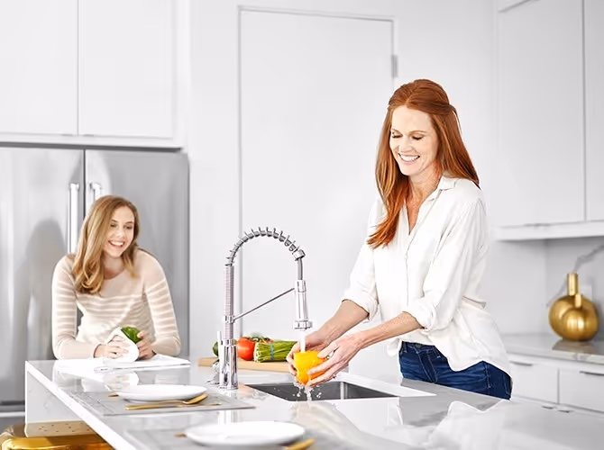 A woman washes dishes in a bright kitchen, surrounded by clean countertops and kitchenware.