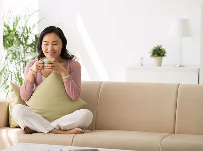 A woman sitting on a couch, holding a cup of coffee, looking relaxed and contemplative.