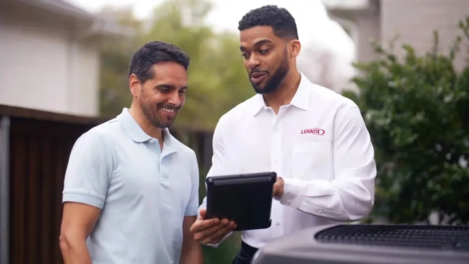 Two men are next to a black air conditioner, engaged in conversation about its operation.