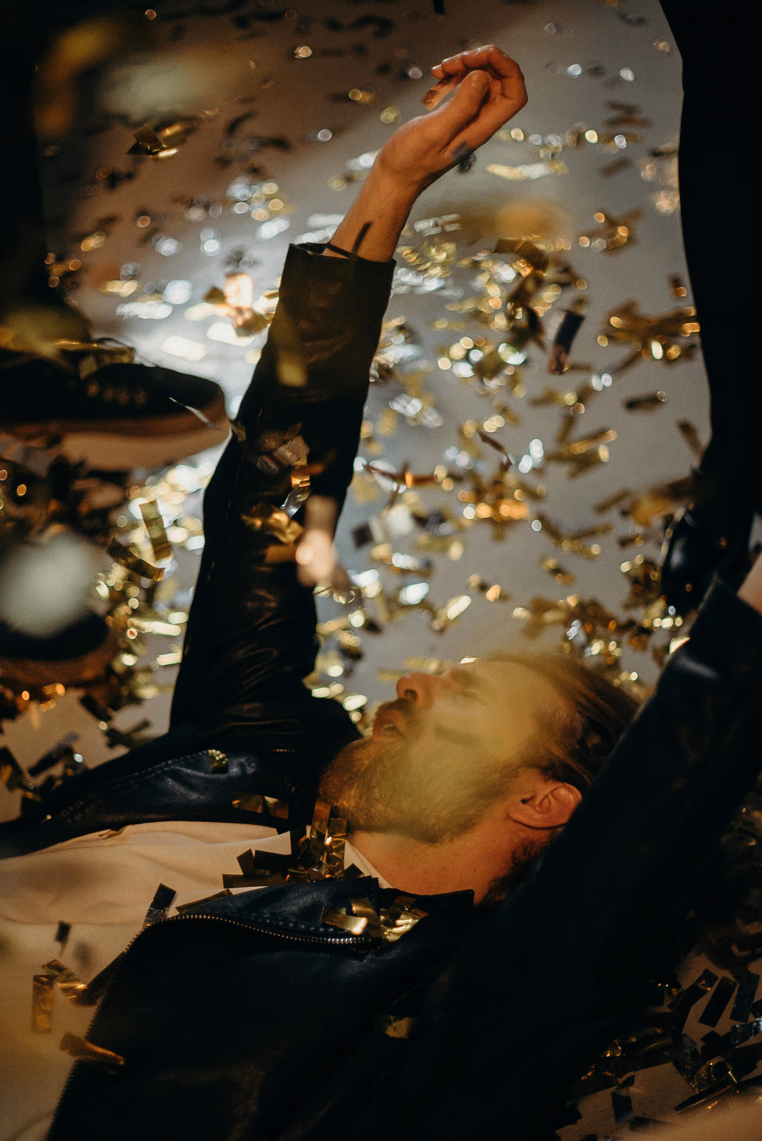 Un homme barbu , les bras levés, entouré de confettis dorés flottants très heureux d'avoir lancé la création de sa micro-entreprise avec Beliive.