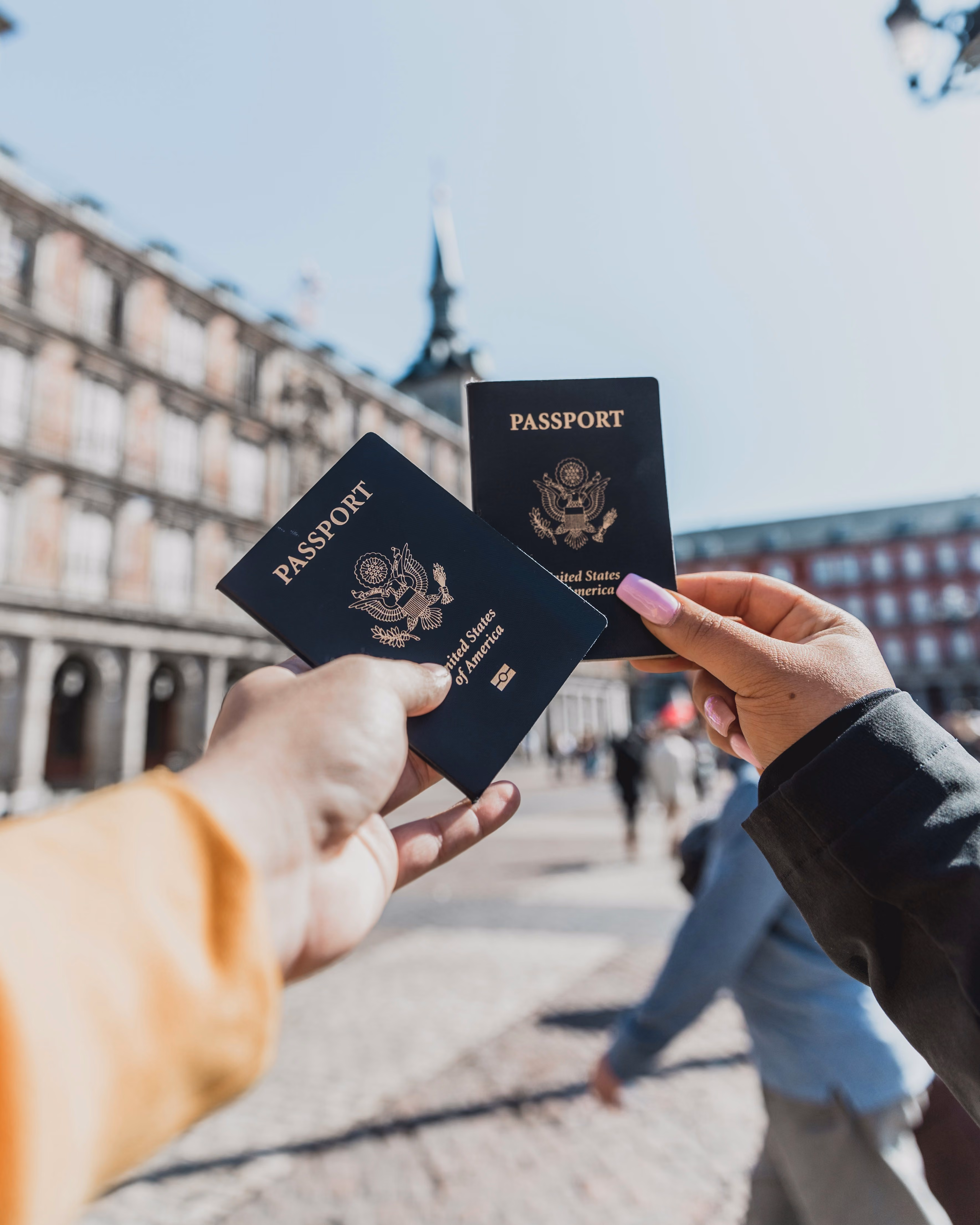 Deux mains tenant ensemble des passeports devant un bâtiment historique en plein air par une journée ensoleillée.
