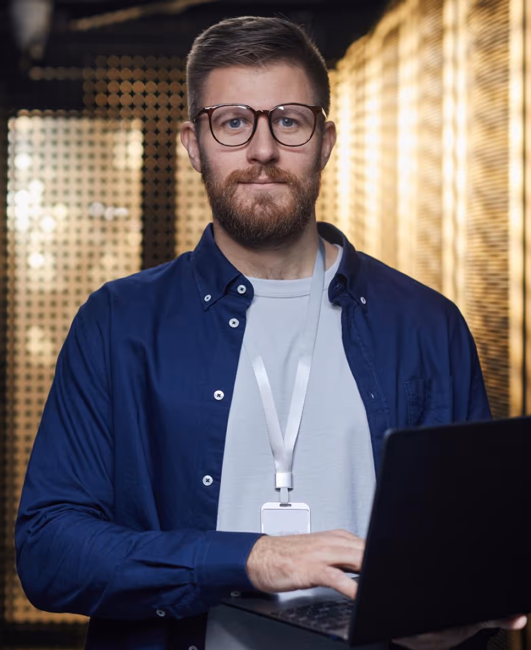 Mann mit Bart und Brille arbeitet an einem Laptop in modern beleuchtetem Raum.