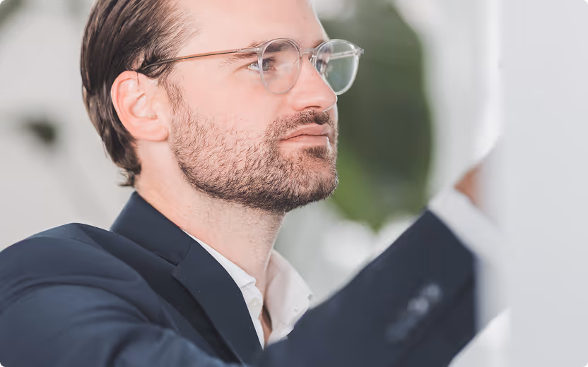 Nahaufnahme eines Mannes mit Brille und Bart, der konzentriert nach rechts schaut.