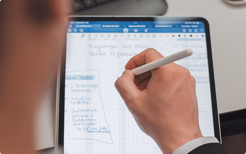 Hand schreibt mit einem weißen Stift auf einem Tablet mit Notizen und Diagrammen.