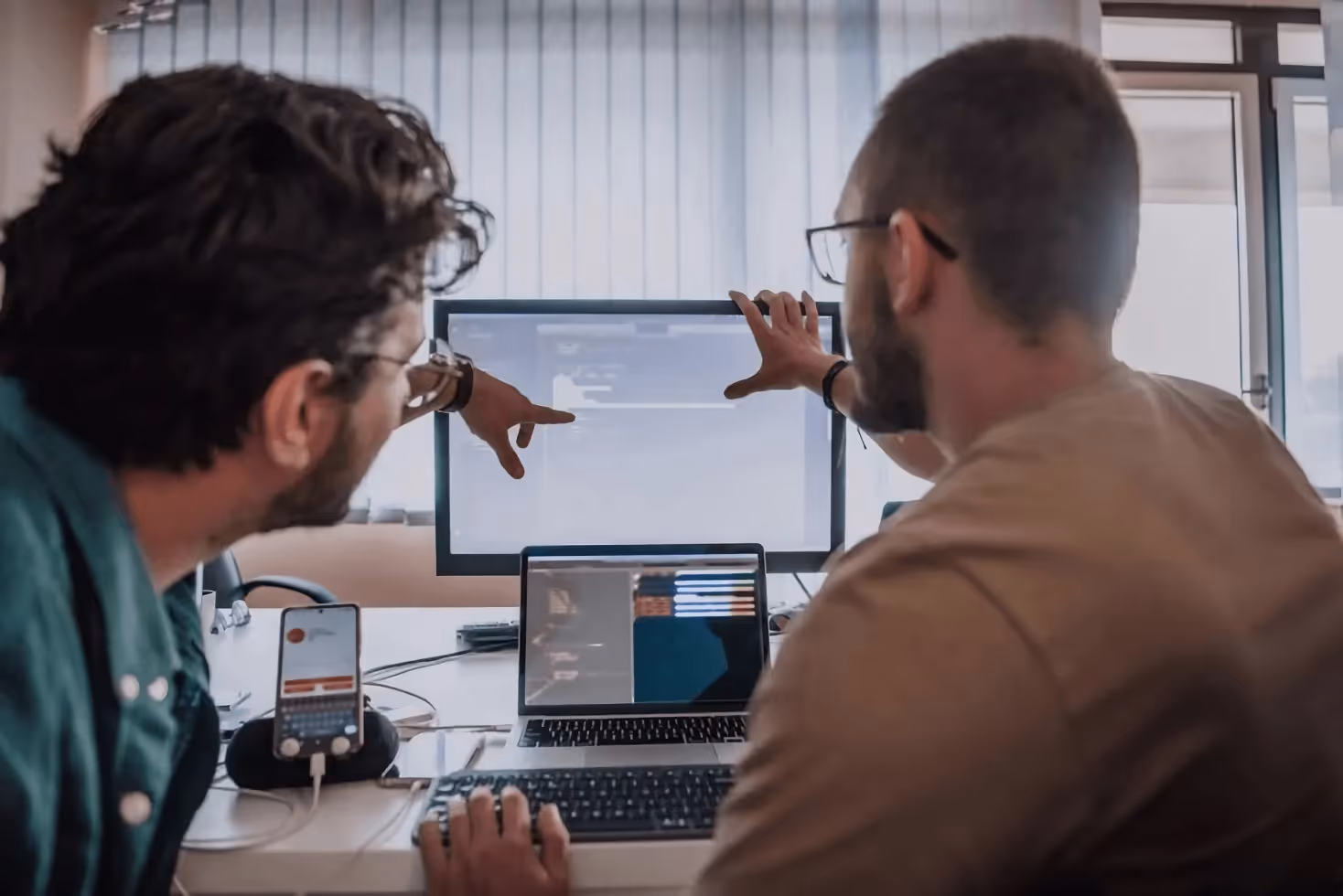 Two mobile app developers focus on a computer in an office.