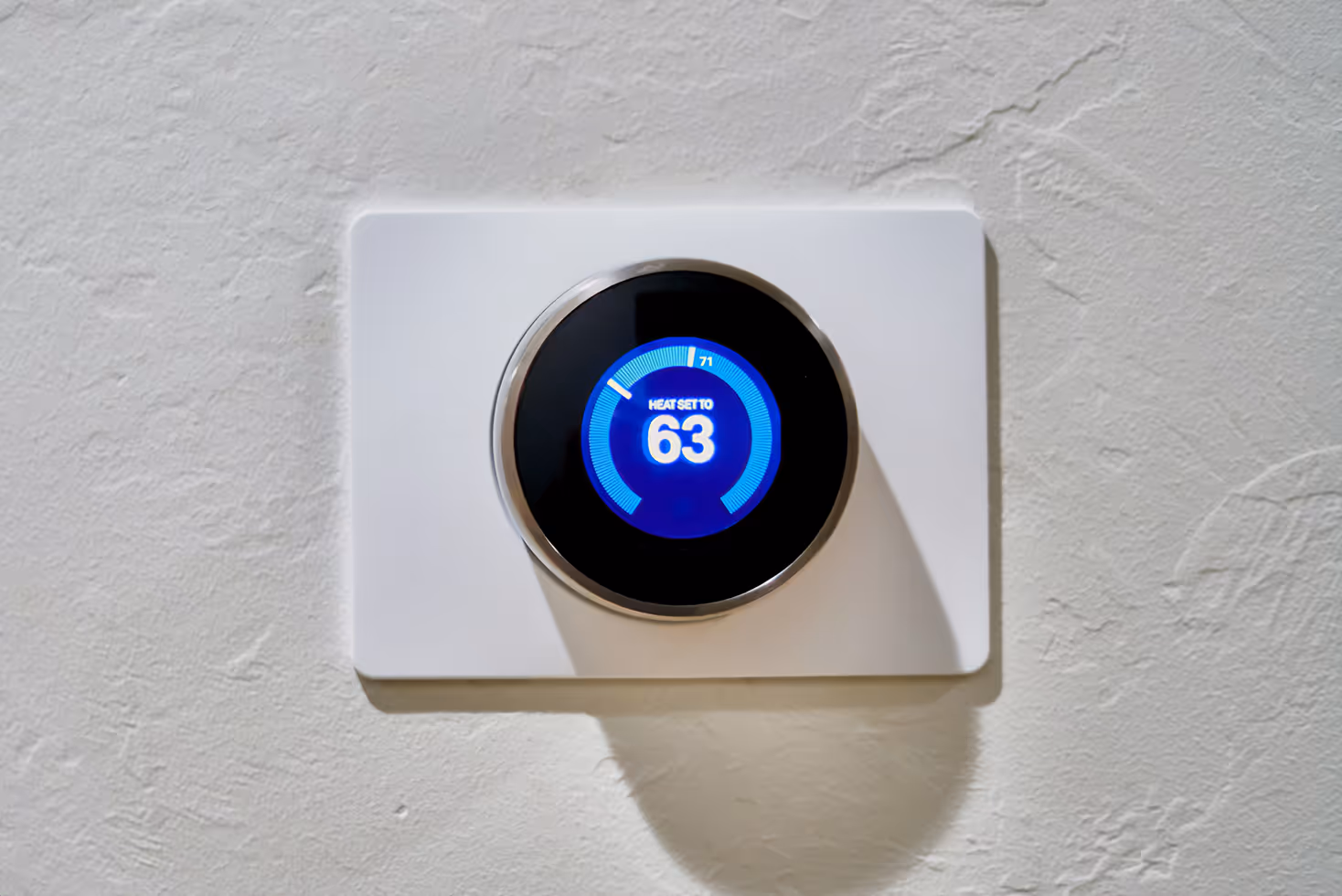 White IoT smart thermostat showing 63 degrees Fahrenheit