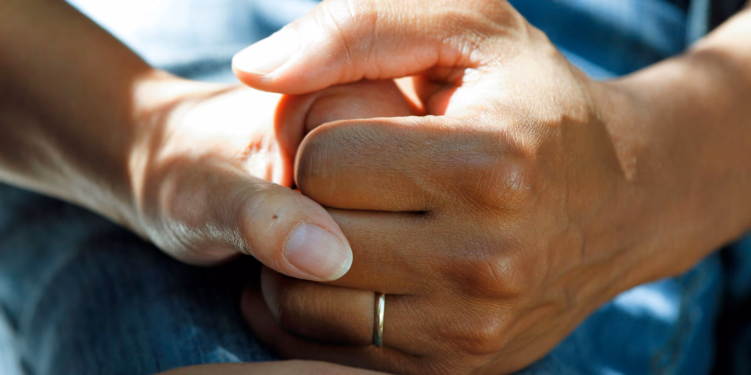 Close-up of two hands gently holding each other, one wearing a wedding ring.