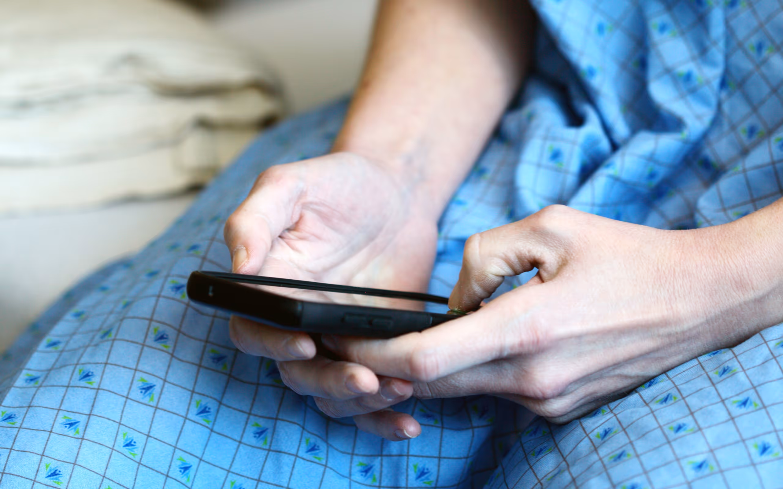 Person wearing a blue patterned hospital gown holding and using a smartphone.