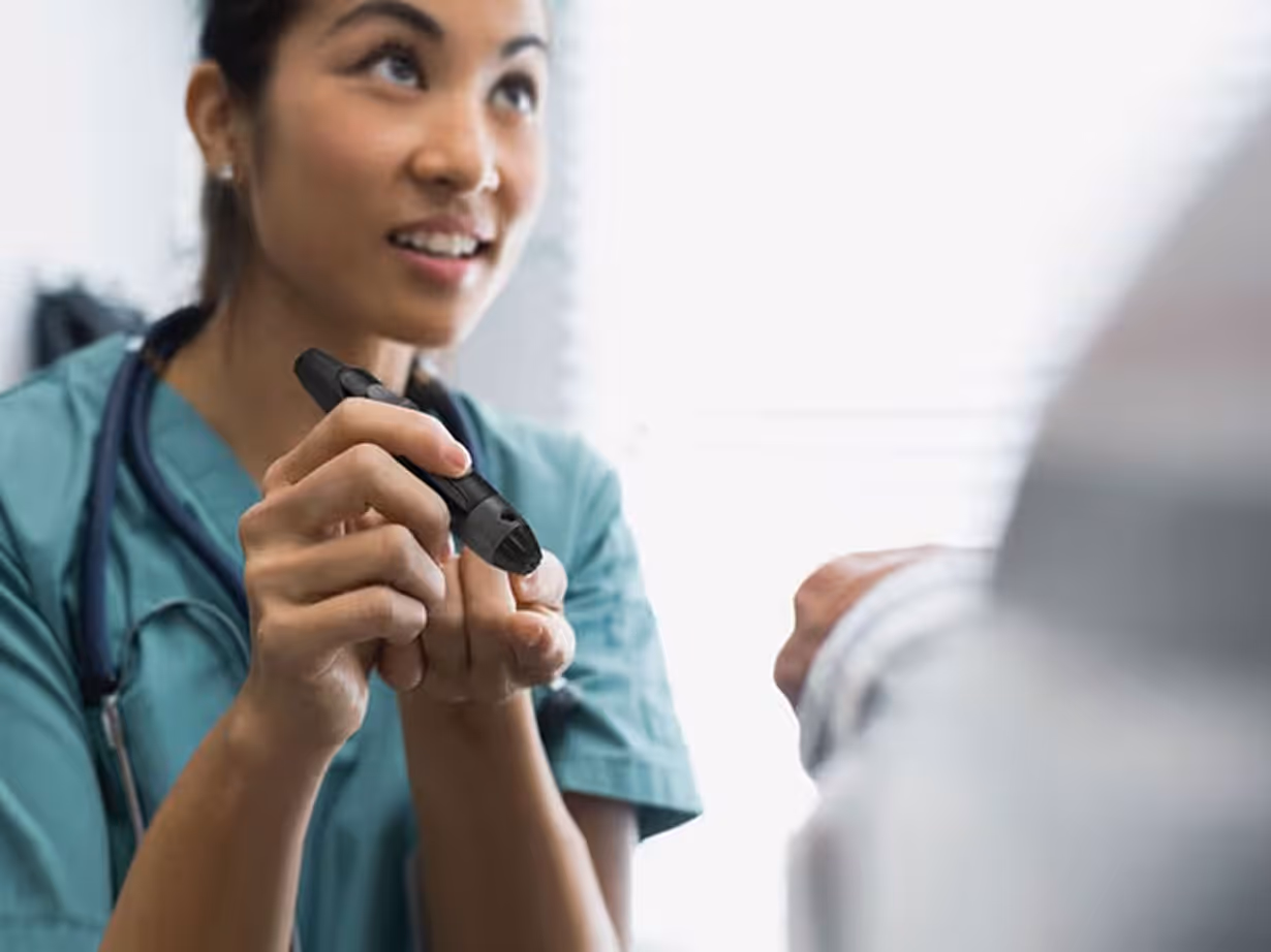 Smiling healthcare professional in scrubs uses a blood glucose meter to check a patient's finger.