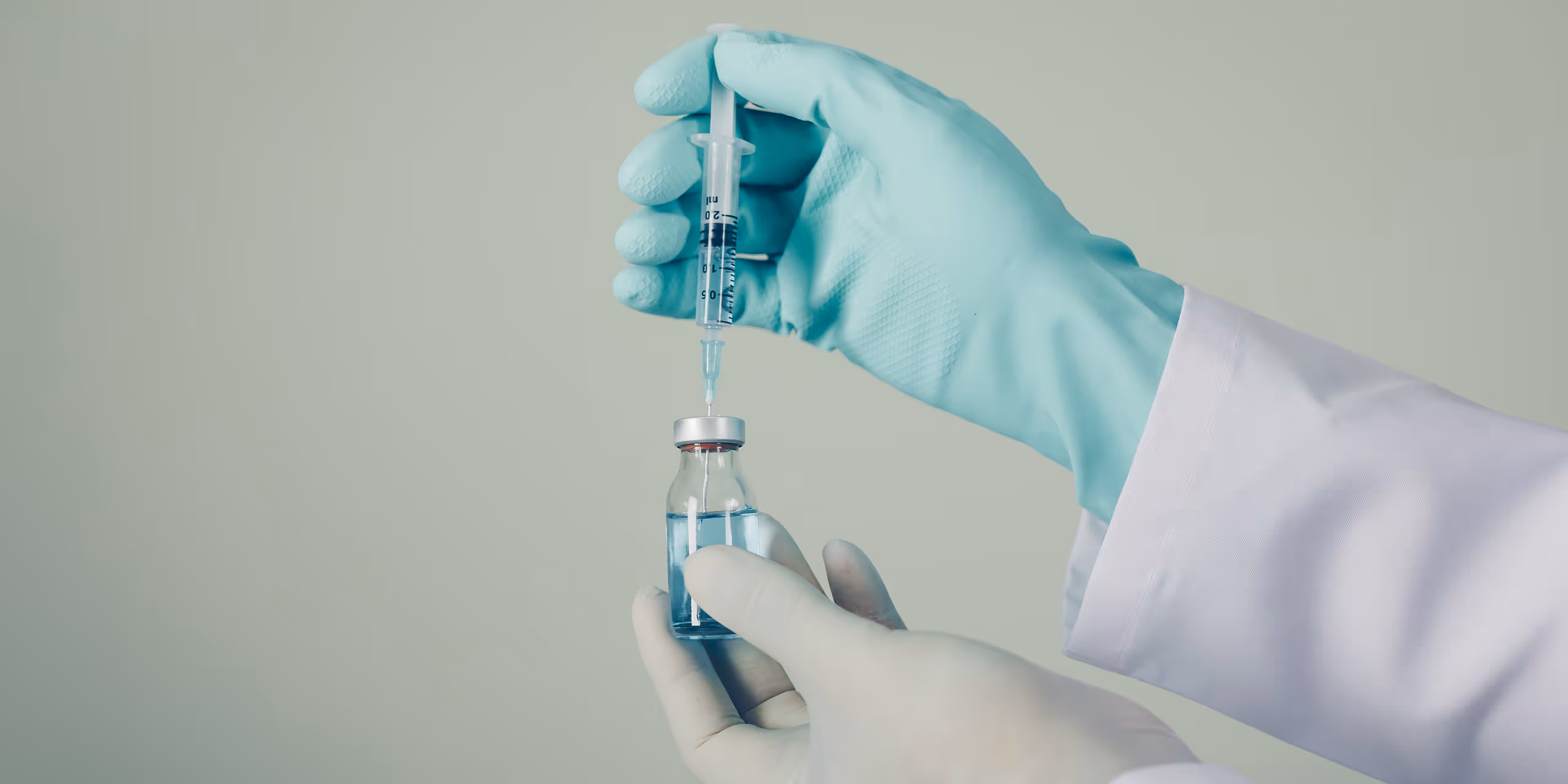 Hands wearing medical gloves holding a vial with blue liquid and drawing liquid into a syringe.