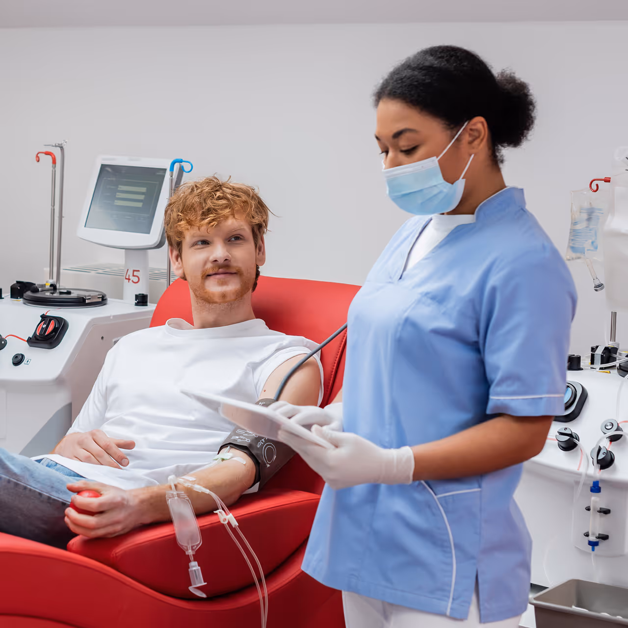 Nurse in medical mask and latex gloves using digital tablet near redhead man with blood.