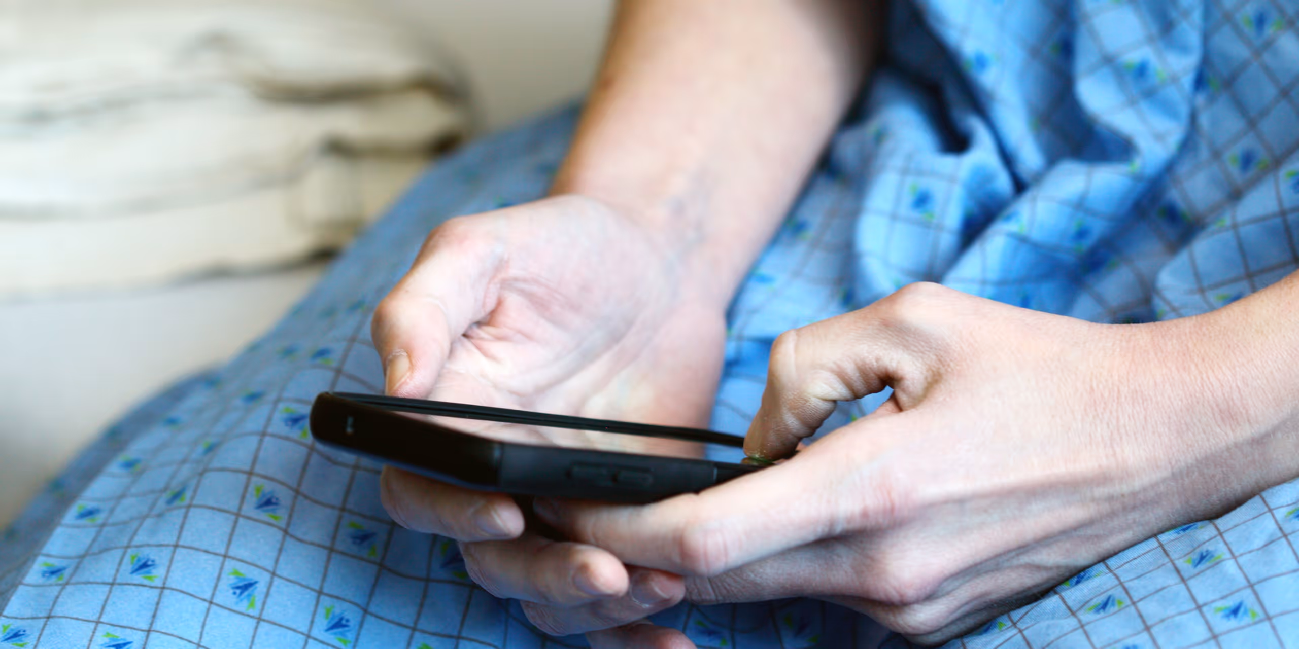 Person wearing a blue patterned hospital gown holding and using a smartphone.