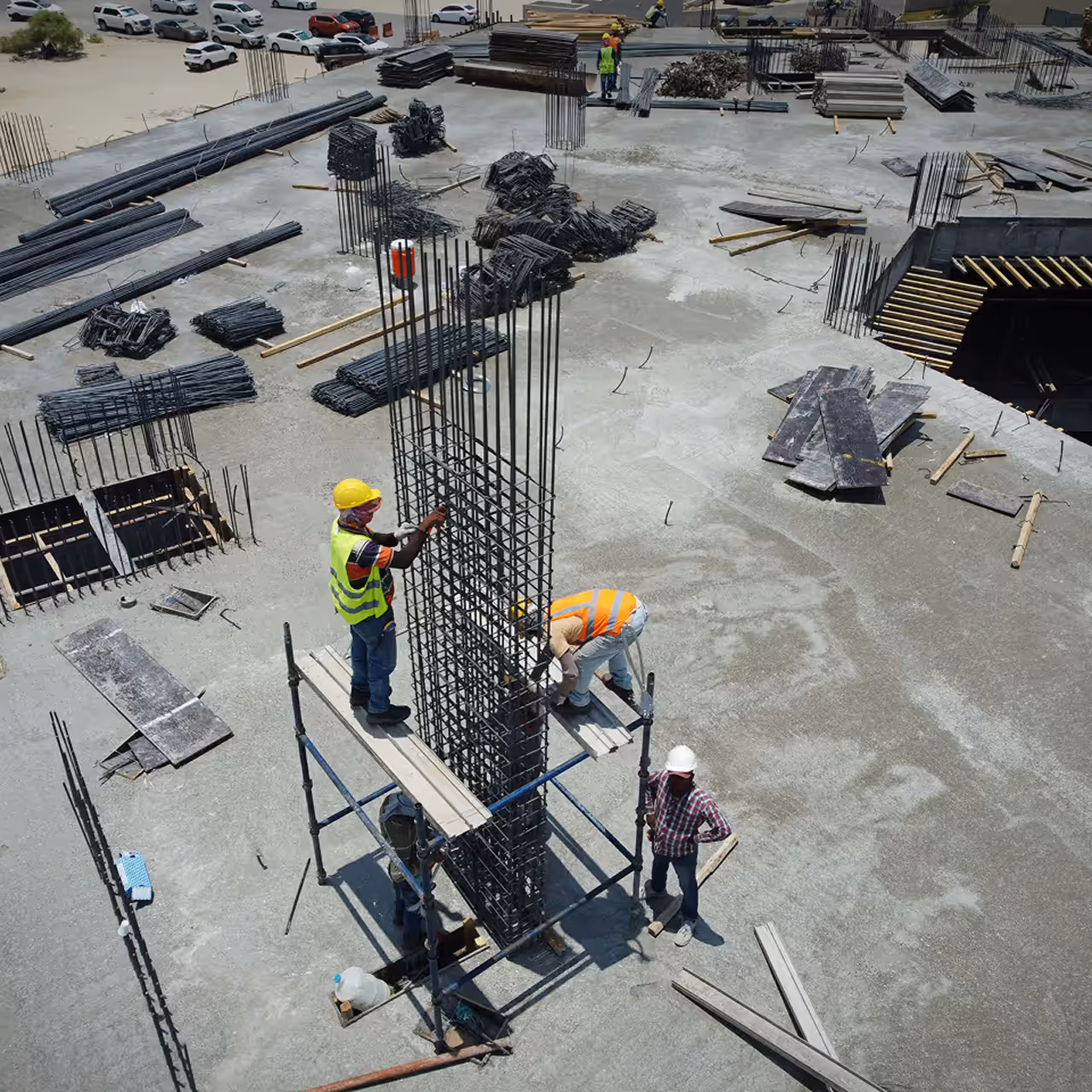 Four construction workers in safety gear assembling steel reinforcement bars on a building site.