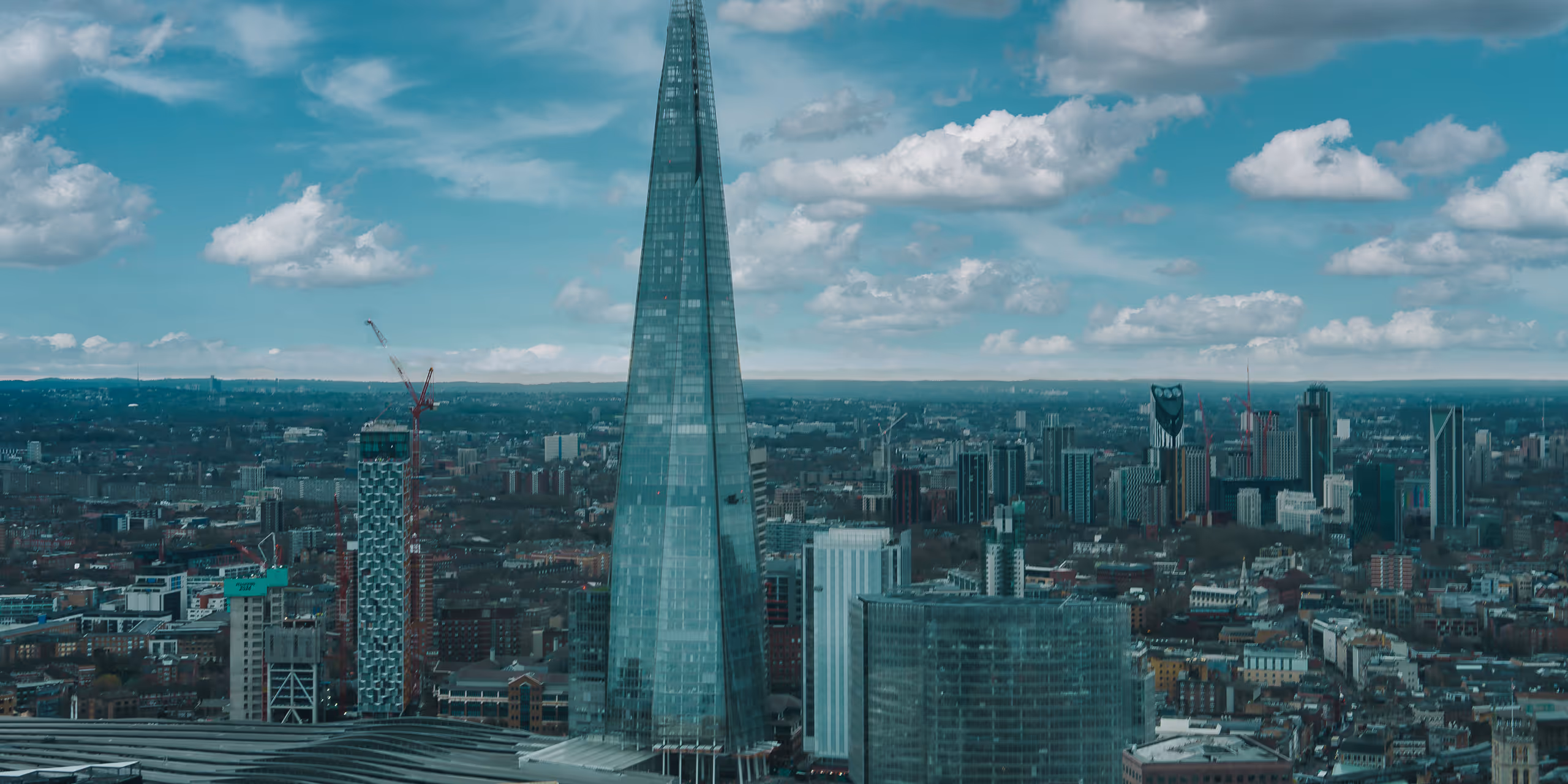 Cityscape of London featuring The Shard skyscraper towering over surrounding buildings under a partly cloudy sky.