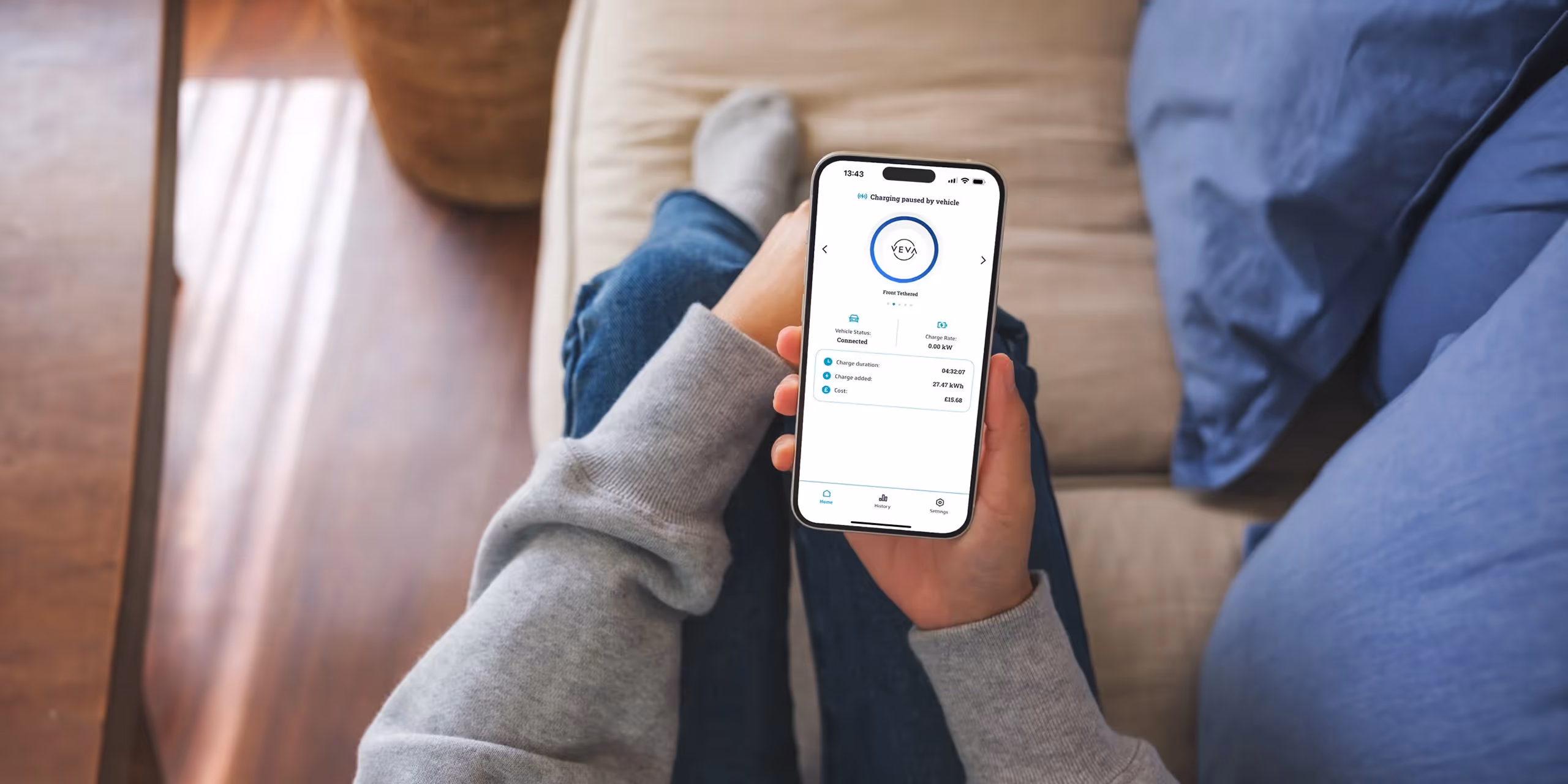 Person holding a smartphone displaying the VEVA app showing vehicle charging paused, status connected, charge duration, added charge, and cost.