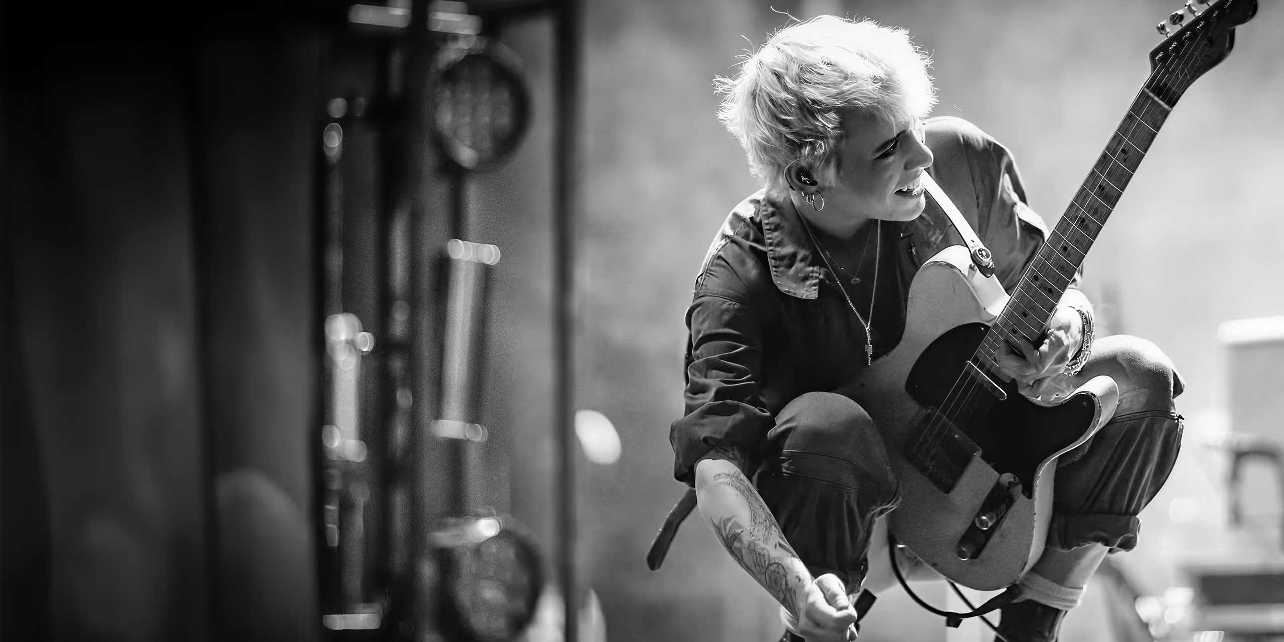 Black and white photo of a musician crouching and playing an electric guitar on stage with a joyful expression.