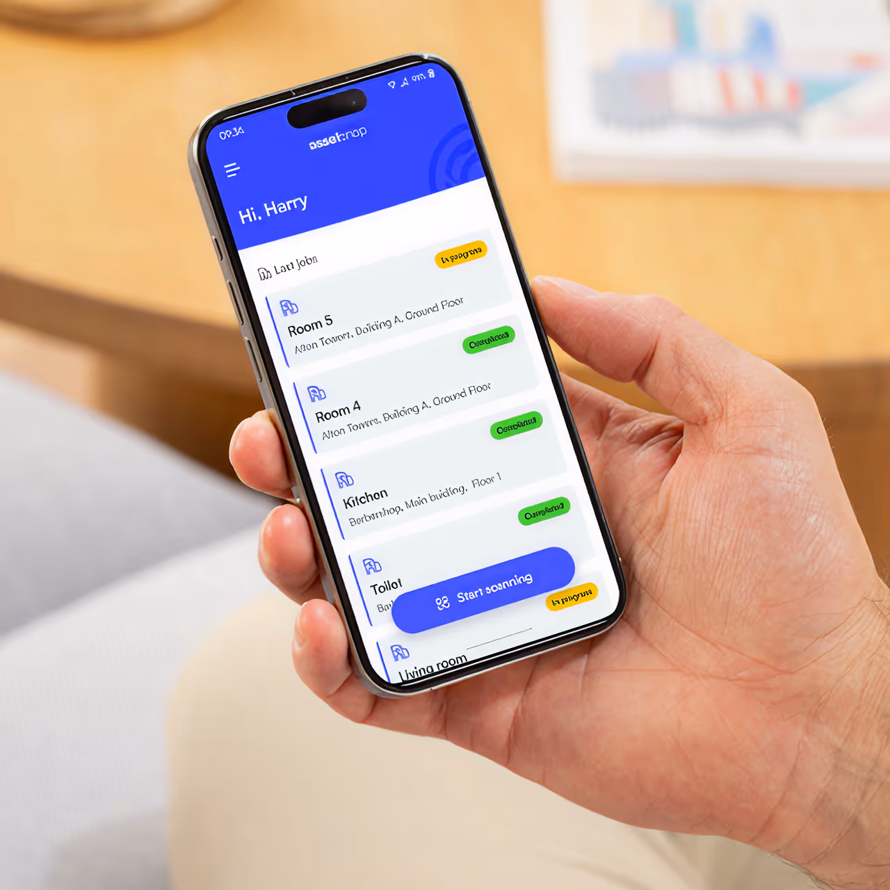 Person holding phone with app showing room names and statuses like completed and in progress.
