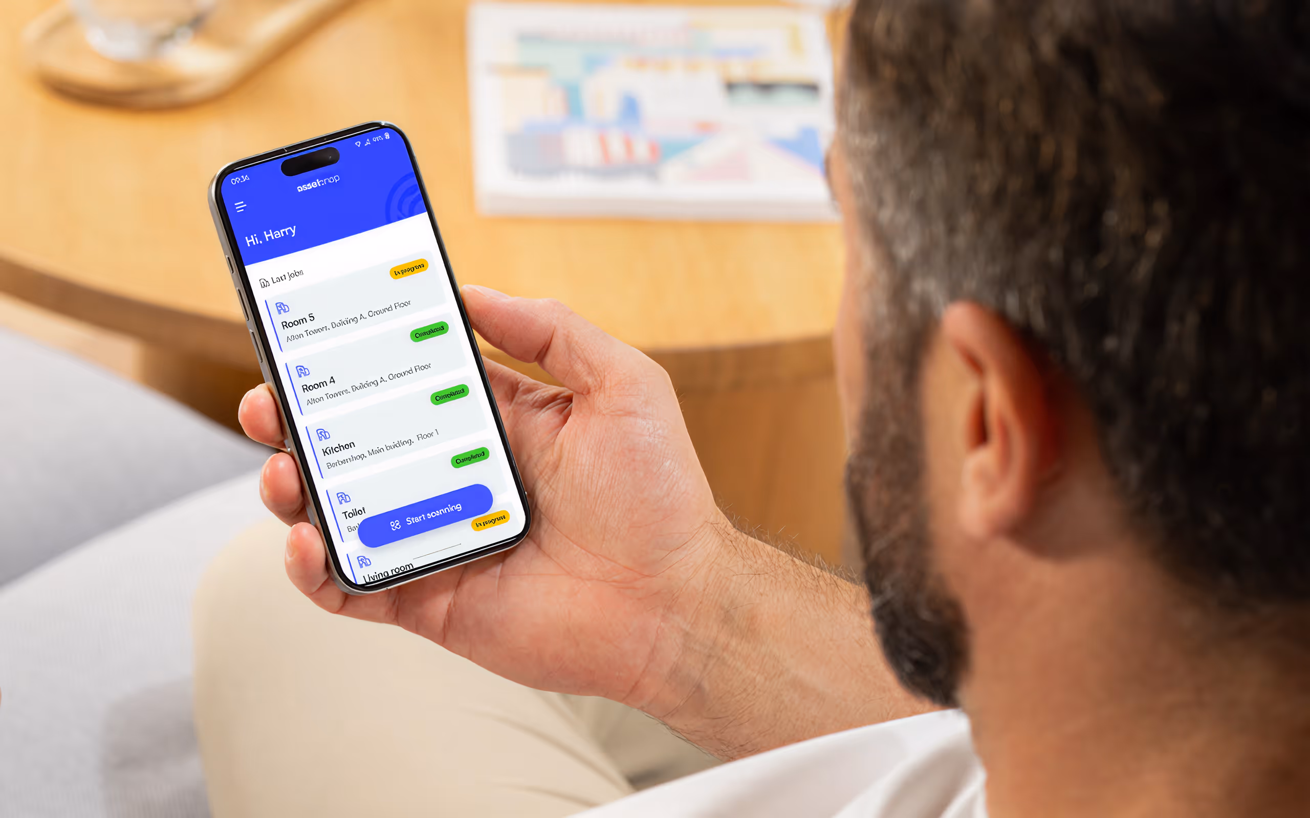 Person holding phone with app showing room names and statuses like completed and in progress.