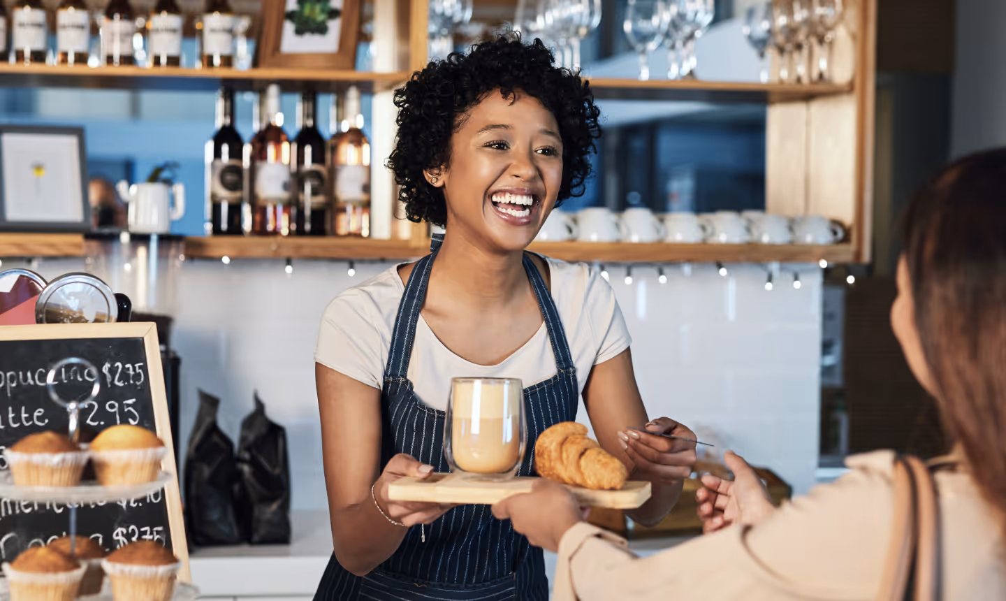 Serveuse dynamique et souriante servant un café avec des pâtisseries dans un établissement chaleureux, incarnant l'excellence du service recherchée dans l'emploi saisonnier de restauration. Cette image illustre parfaitement l'ambiance conviviale des jobs saisonniers en service. Le travail saisonnier en salle permet de développer des compétences relationnelles exceptionnelles et une expertise du service à la française. Les emplois saisonniers logés dans la restauration offrent une formation complète : prise de commande, service, connaissance des produits et relation client. L'emploi saisonnier de serveuse combine technique professionnelle et contact humain dans un environnement stimulant. Découvrez tous les postes de service saisonnier sur Ohmyseason.fr.